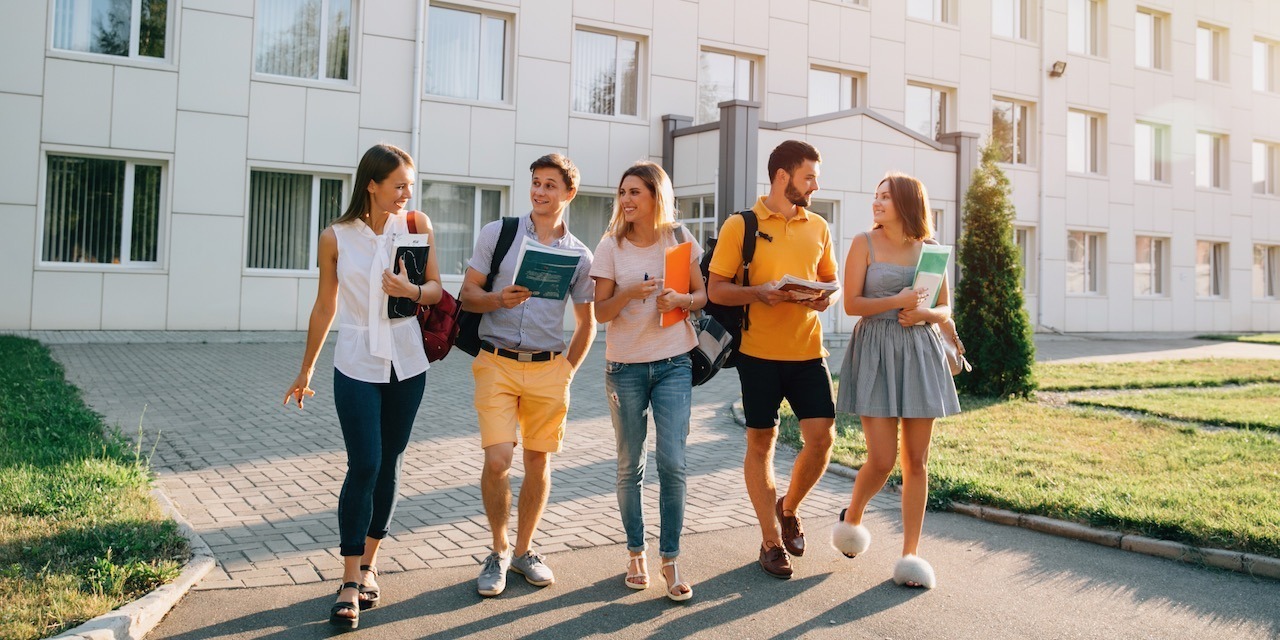 Five friendly students are walking after they passed test outside the college building and discuss the project